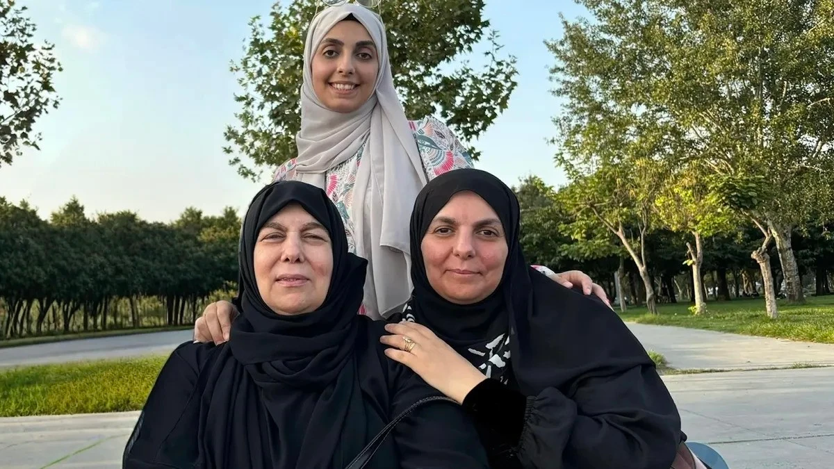 Three-generation Syrian families sits together in a park. The grandmother, a survivor of the 1982 Hama massacre, is seated on the left, with her daughter beside her and her granddaughter standing behind them. They participated in a study examining the biological inheritance of trauma.