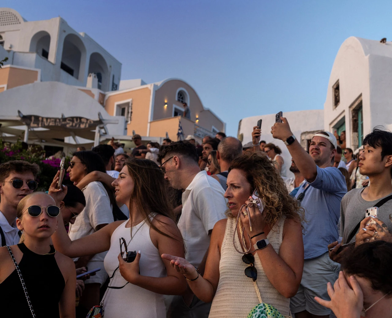 Tourists in Santorini, Greece, on July 25, 2024, holding their phones and facing the sun.