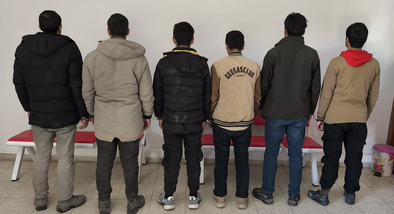 A group of 6 migrants, facing away, are captured after entering the country illegally