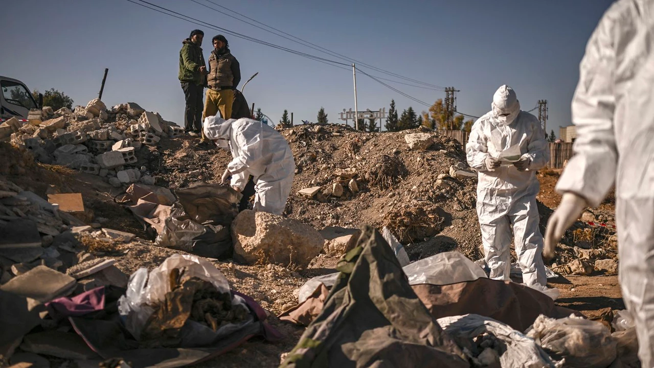 Photo shows Members of Syria's White Helmets civil defense collect human remains at a mass grave that was uncovered in Damascus