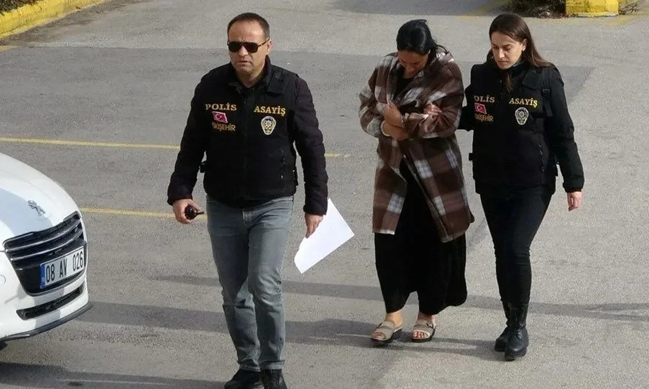 A woman in a plaid coat being escorted by two police officers outside a building.