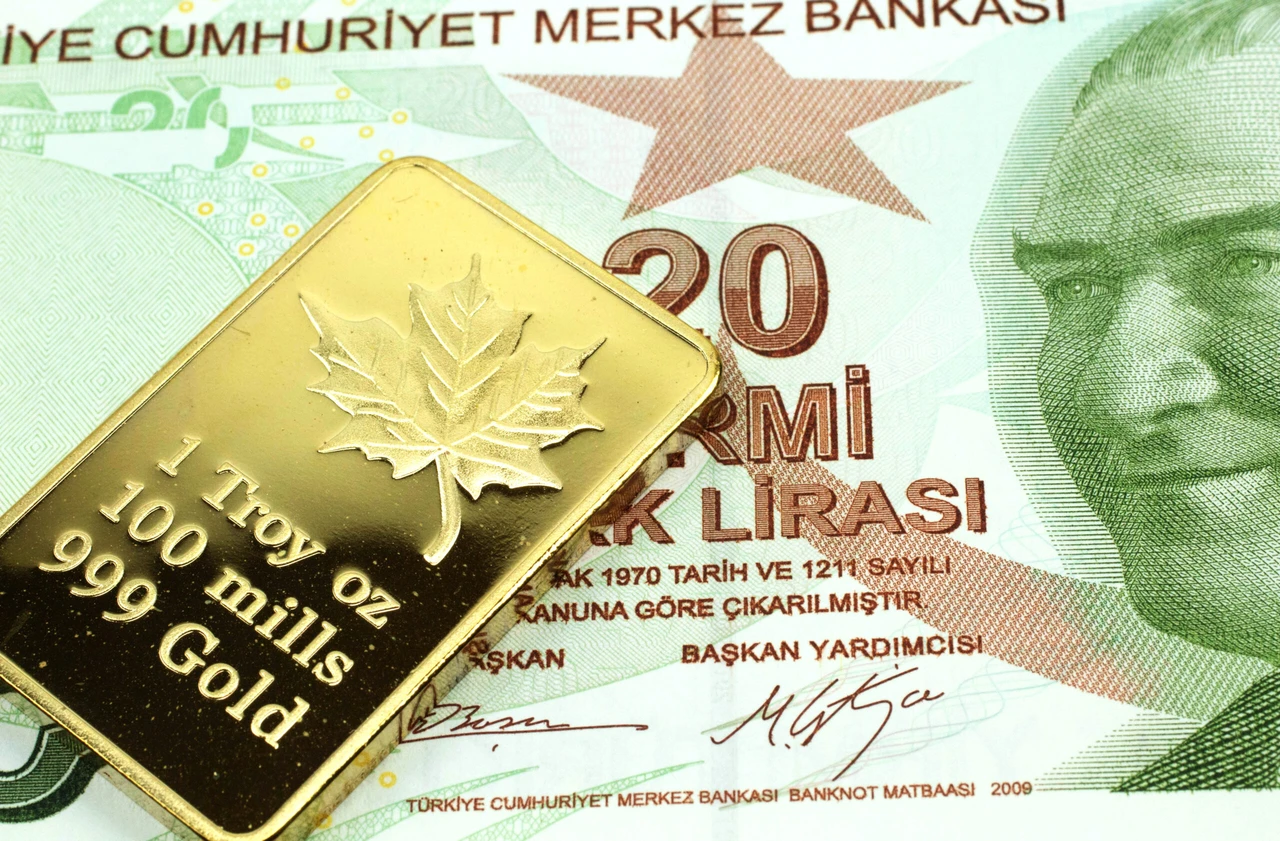 Close-up of a 1 Troy ounce gold bar with a maple leaf design resting on a 20 Turkish lira banknote