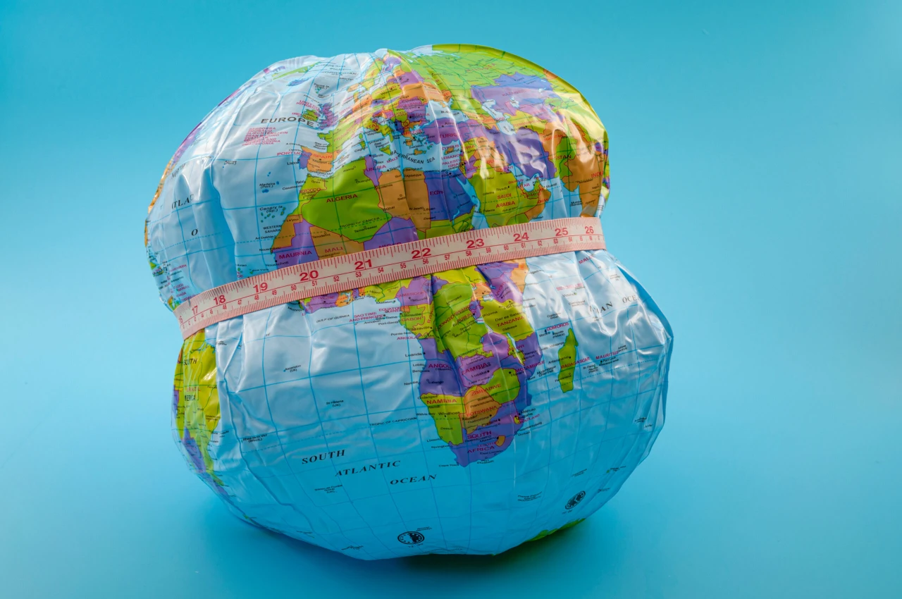 An inflated and compressed world globe with a measuring tape around its middle, representing the increasing global obesity epidemic and its widespread impact.