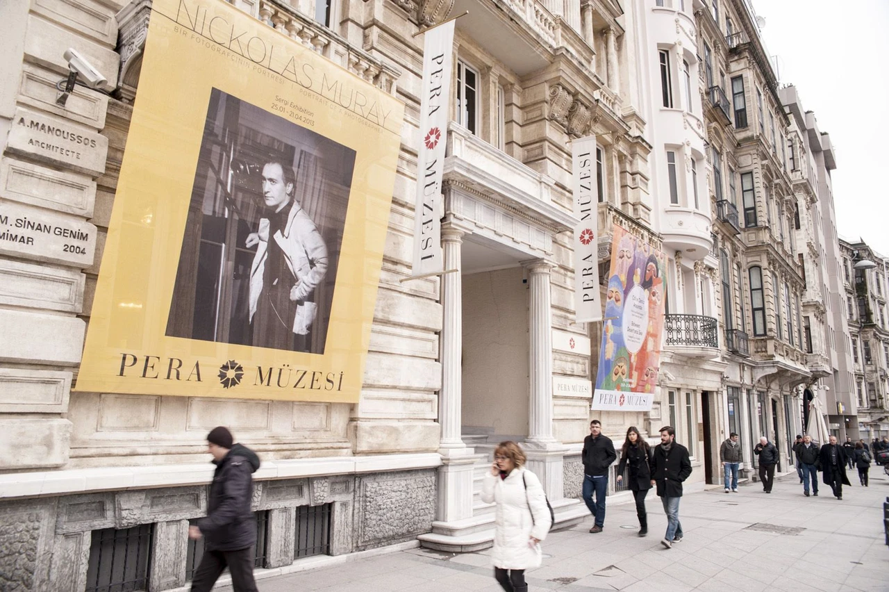 Exterior of Pera Museum in Istanbul, Turkey, with exhibition banners on the building's facade and pedestrians walking along the sidewalk.