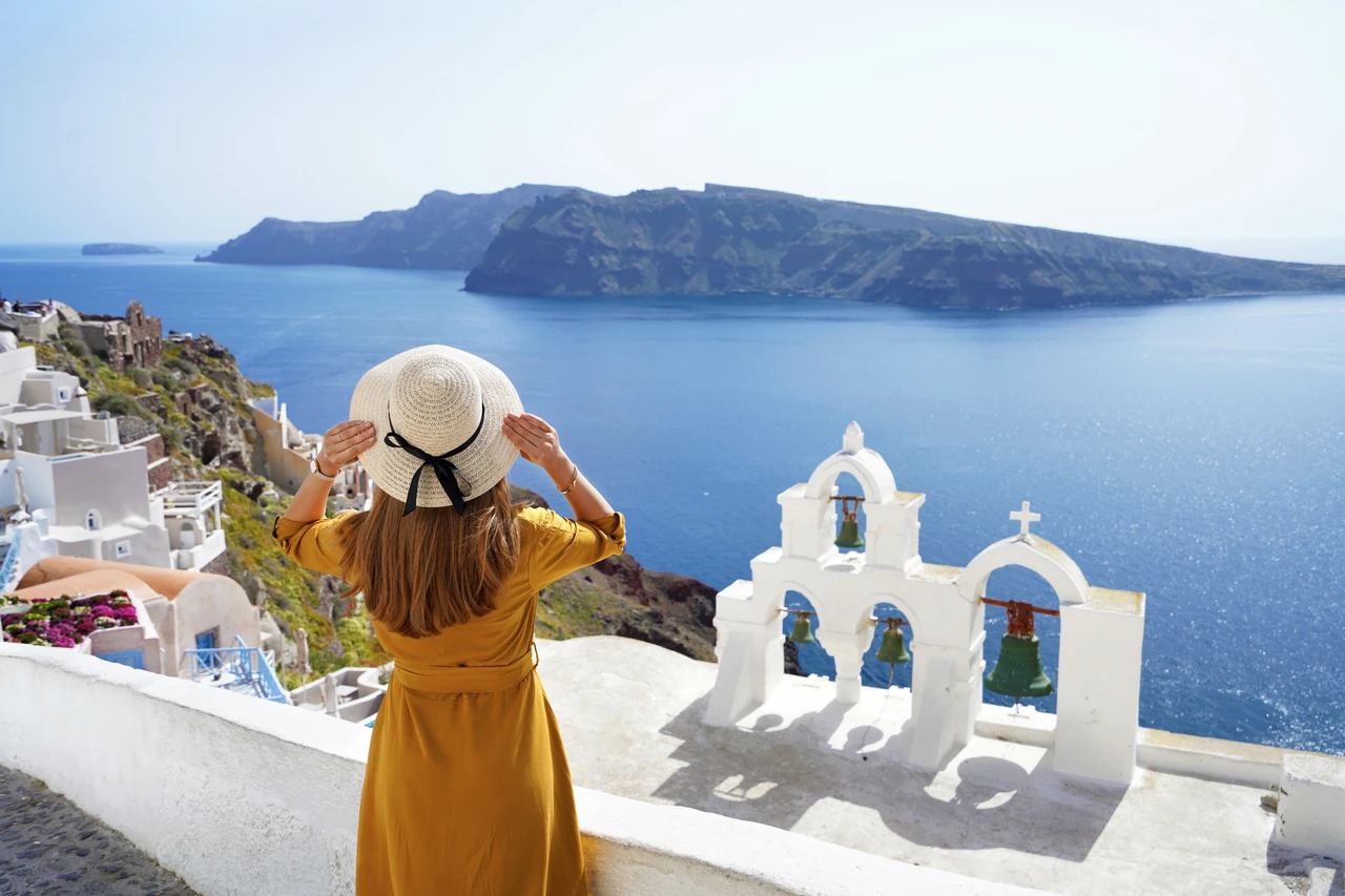 A young woman stands with her back to the camera, admiring the stunning view of Oia’s whitewashed buildings and the deep blue Aegean Sea in Santorini, Greece.