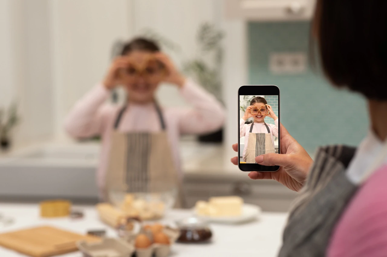 Woman photographing little girl in an apron making cookie dough in the kitchen.