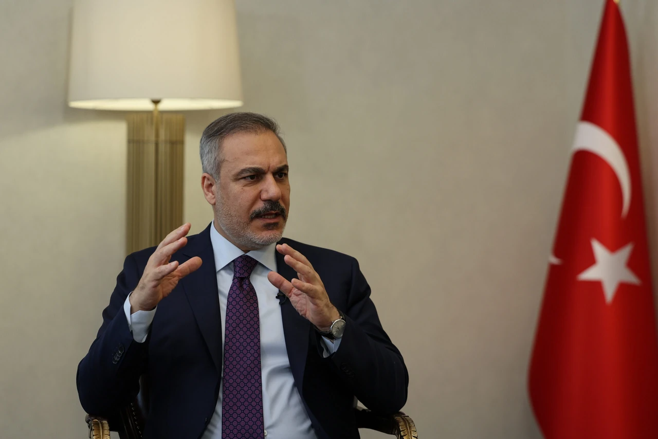 photo shows Turkey Foreign Minister Hakan Fidan speaking with a Turkish flag next to him