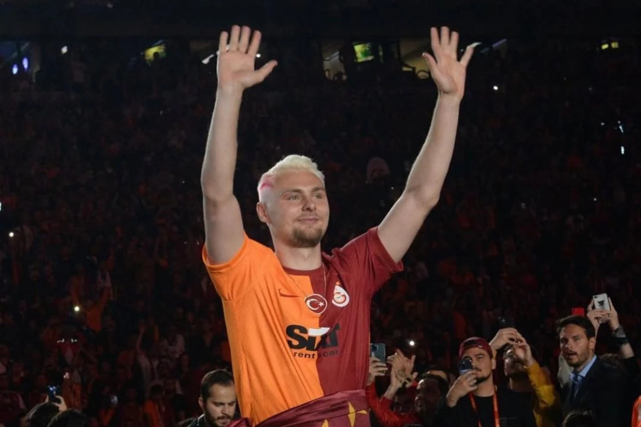 Victor Nelsson raises both hands while wearing Galatasaray's orange and red jersey