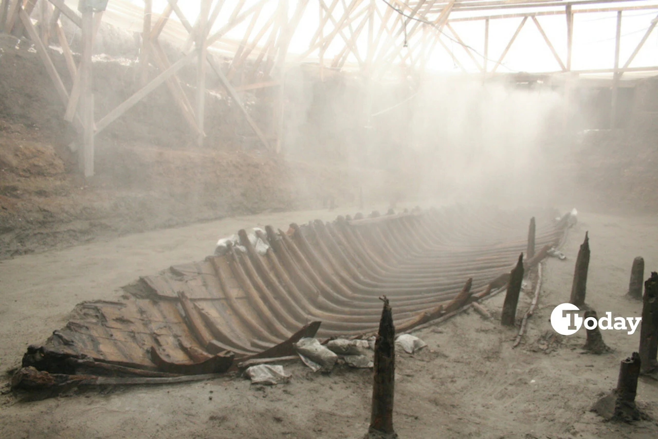 A shipwreck's keel, discovered during the Yenikapı metro construction, emerges from the excavation site, enveloped in mist.