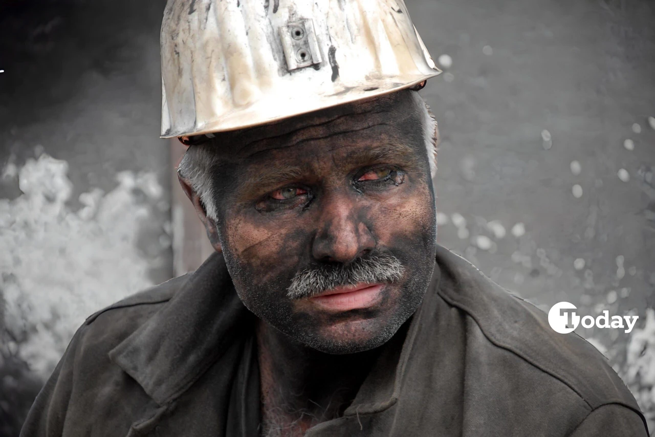 A grieving miner in Kilimli, Zonguldak, Türkiye, wipes coal dust from his face as he waits for his two colleagues trapped in a mine collapse. His face shows deep sorrow and exhaustion.