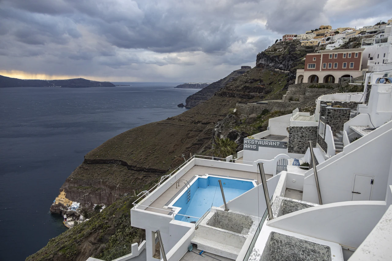 Empty pools with stagnant water in Fira, Santorini, where halted construction projects remain abandoned.