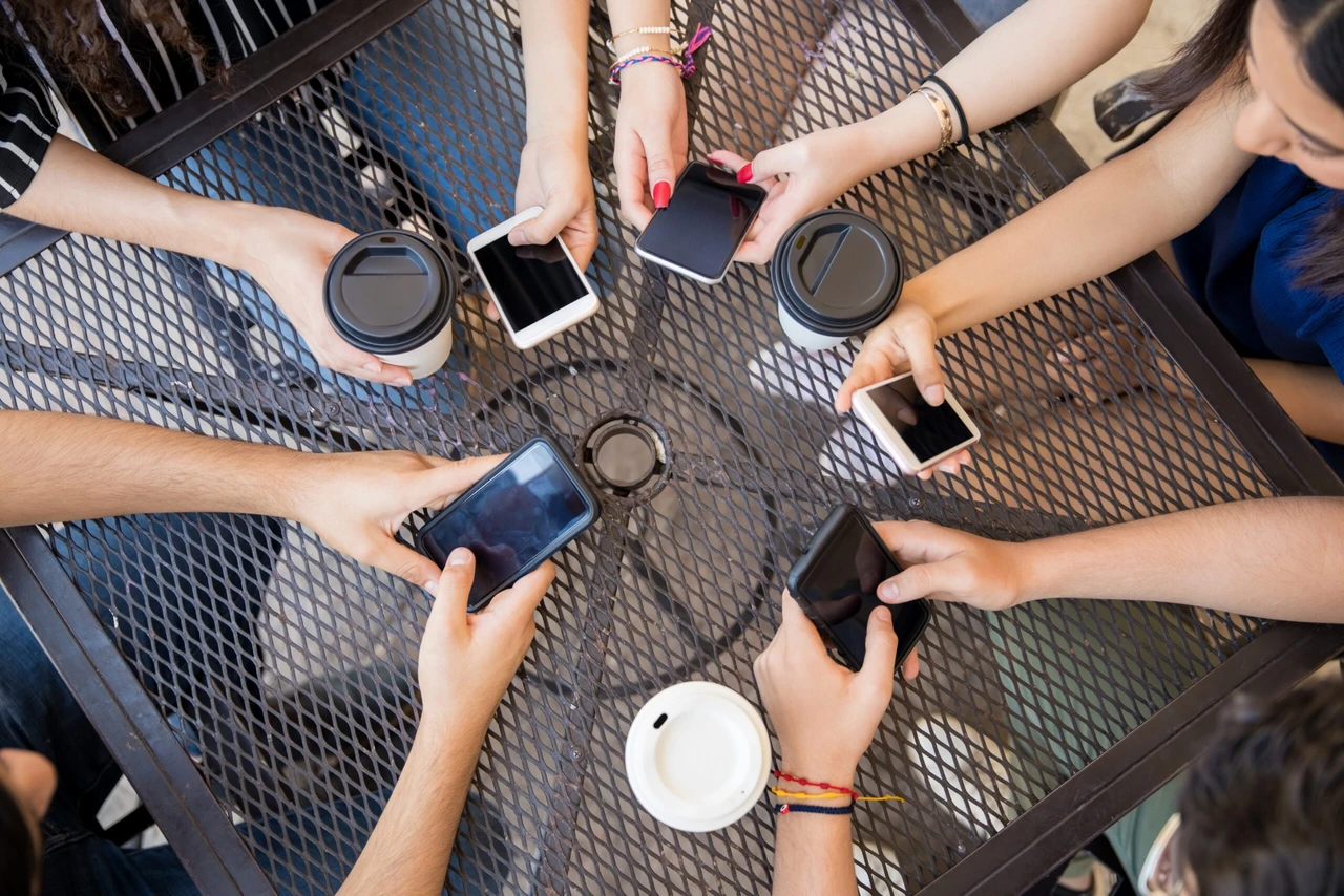 A top view of young friends' hands using mobile phones while sitting at a cafe.