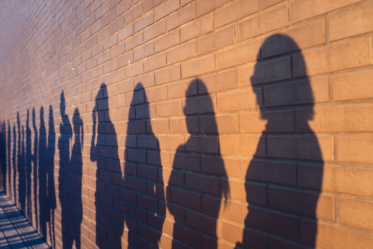 People crowd shadows lined up against a red brick wall