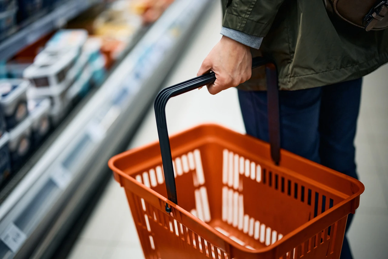 Person holding an empty orange shopping basket in a grocery store aisle