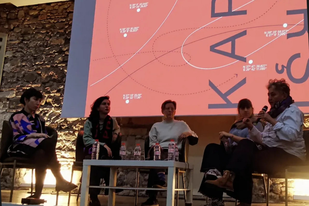 A panel discussion at the Karsi/Καρσί Izmir Gathering, featuring five speakers seated in front of a large screen displaying the event's visual design