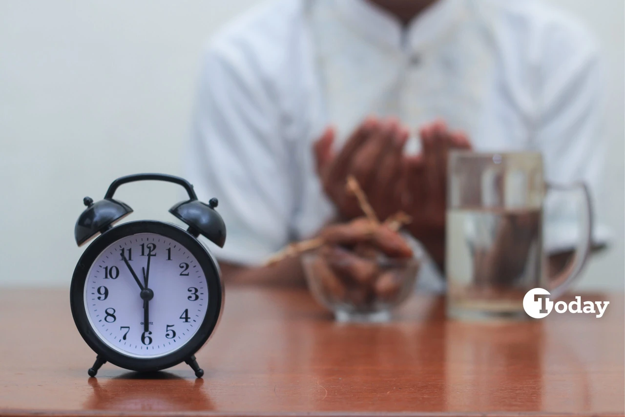 Table clock showing 6 p.m. with an Asian man's hand praying in the blurred background.