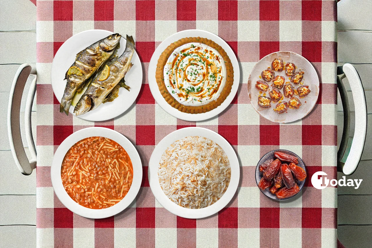 A traditional Turkish iftar meal set on a red and white checkered tablecloth, including oven-baked whole fish with lemon, a bowl of green lentil and noodle soup, a plate of spicy red lentil dip with olive oil, a dish of rice pilaf with vermicelli, and a dessert of stuffed dates with walnuts and tahini.