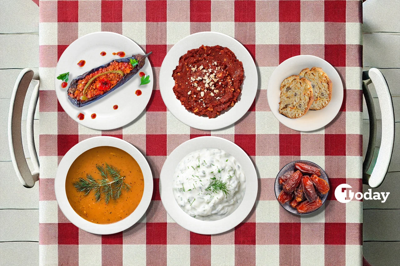 A Turkish iftar spread on a checkered tablecloth, showcasing Karniyarik (stuffed eggplant), Muhammara (spicy red pepper and walnut dip), Tarhana soup, Cacik (cucumber and dill yogurt dip), carrot and cinnamon cake, and a plate of dates.