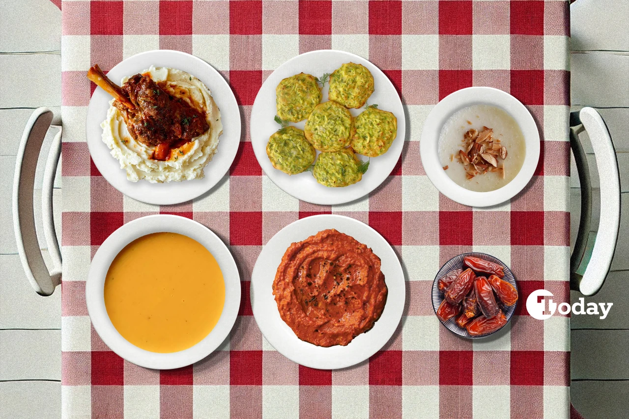 A traditional Turkish iftar meal laid out on a checkered tablecloth, including pumpkin soup, zucchini fritters, roasted lamb shank over mashed potatoes, roasted red pepper and walnut dip, almond pudding with toasted nuts, and a side of dates.