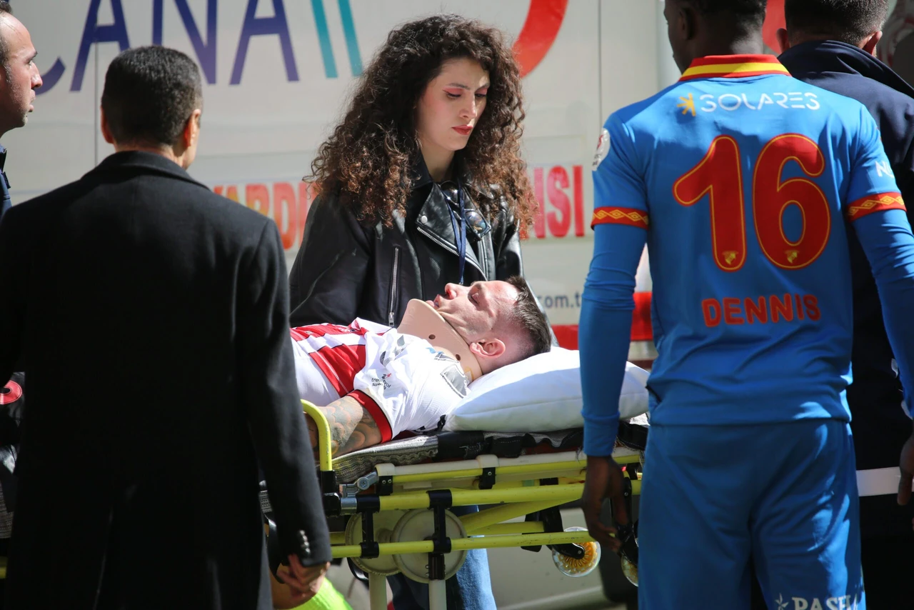 A footballer lies on a stretcher being carried towards an ambulance