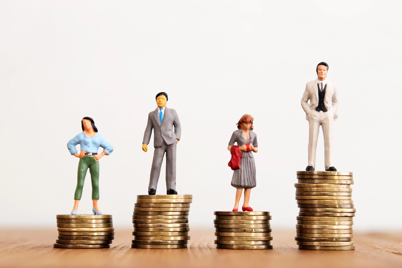 Turkish women - Miniature figurines of men and women standing on different heights of stacked coins, illustrating the gender wage gap and economic inequality.