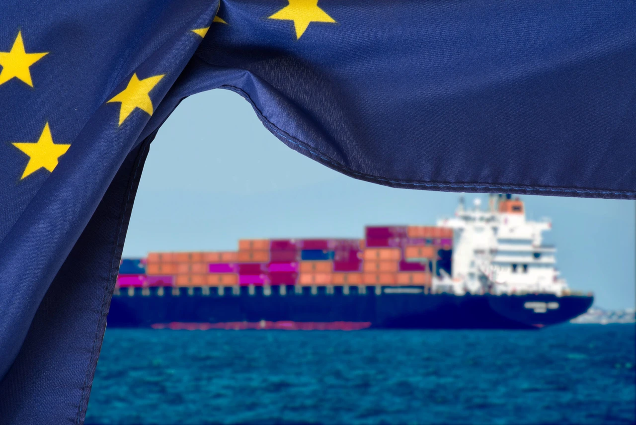 A cargo ship loaded with containers sails under the European Union flag