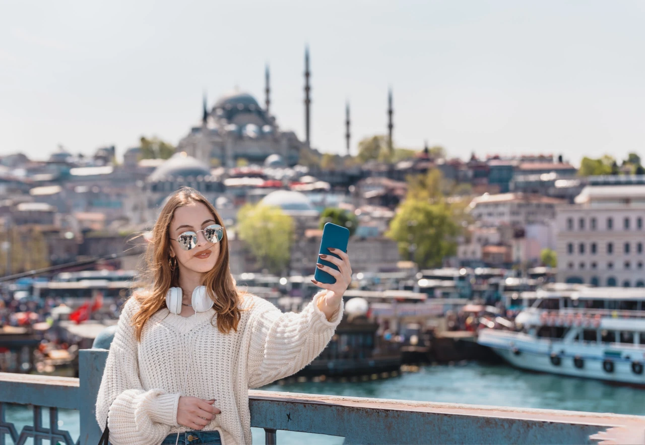 Portrait of a young women with headphones,smartphone and sunglasses takes selfie on Galata Bridge with view of Suleymaniye Mosque in Istanbul, Turkey