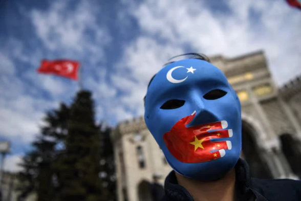 Photo shows man wearing uyghur flagged masked with chinese flagged hand covering his mouth