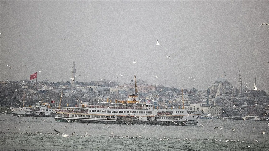 A ferry sails through the Bosphorus in Istanbul amid snowfall, with the city's historic skyline, mosques, and seagulls visible in the background