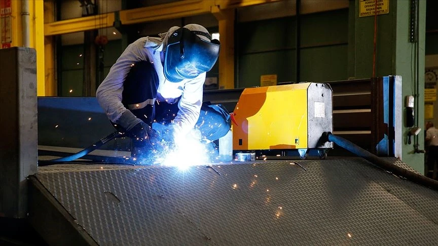 The photo shows a worker in protective gear welding at an industrial facility