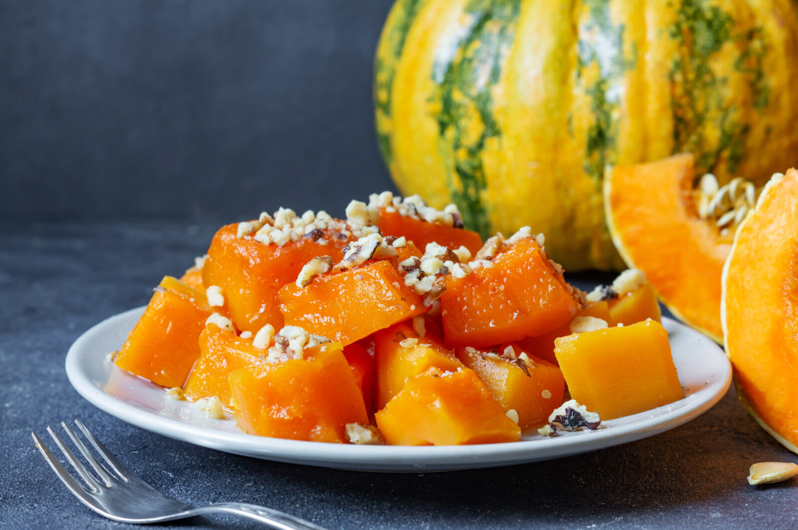 iftar menu dessert - pumpkin dessert on white plate dressed with crushed walnuts and tahini