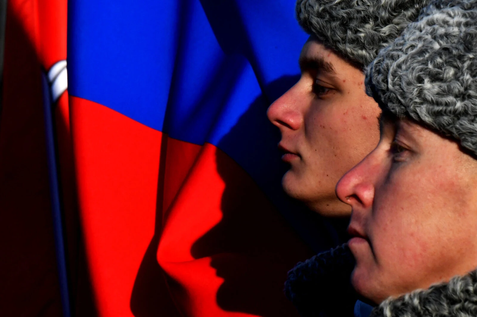 Photo shows close up shot of Russian soldiers' faces in front of a Russian flag