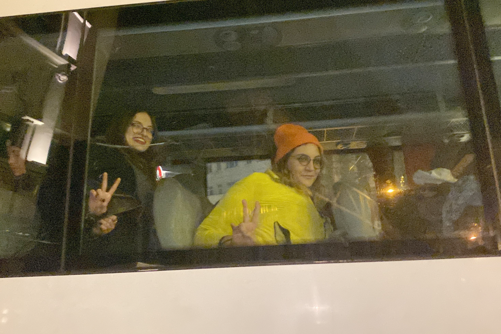 Two detained young women make peace signs while handcuffed with plastic restraints inside a police vehicle in Istanbul, Türkiye