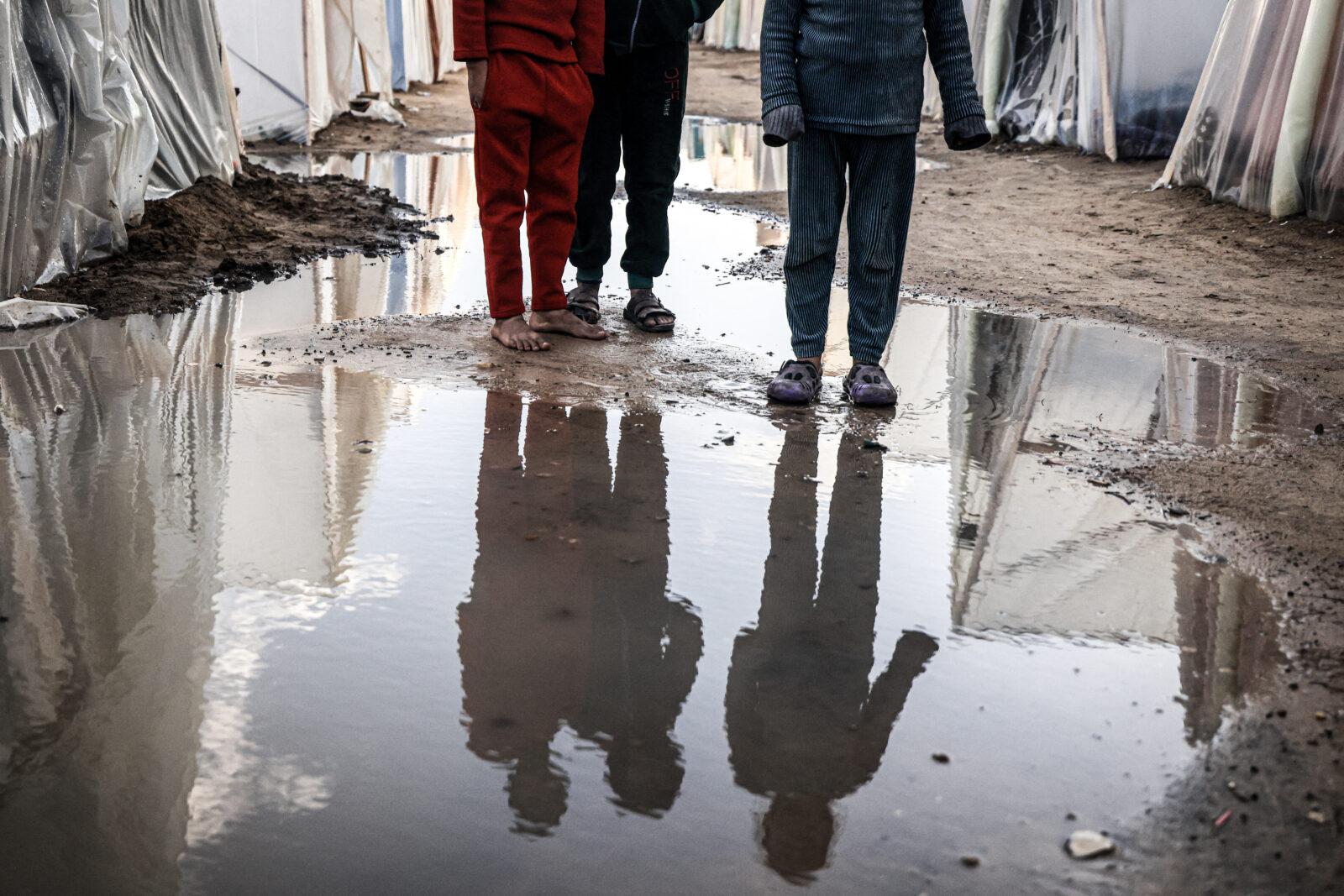 Displaced Palestinian children in Gaza stand amid tents flooded by heavy rain.