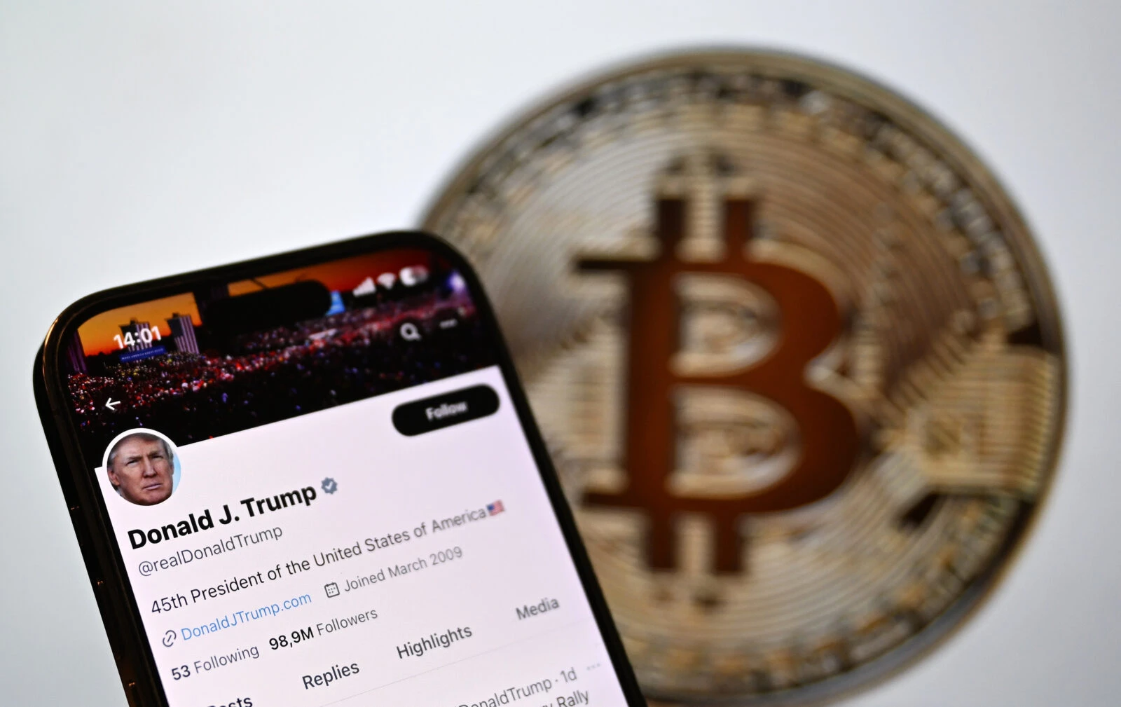 A mobile phone screen displays U.S. President Donald Trump's X account in front of Bitcoin's logo