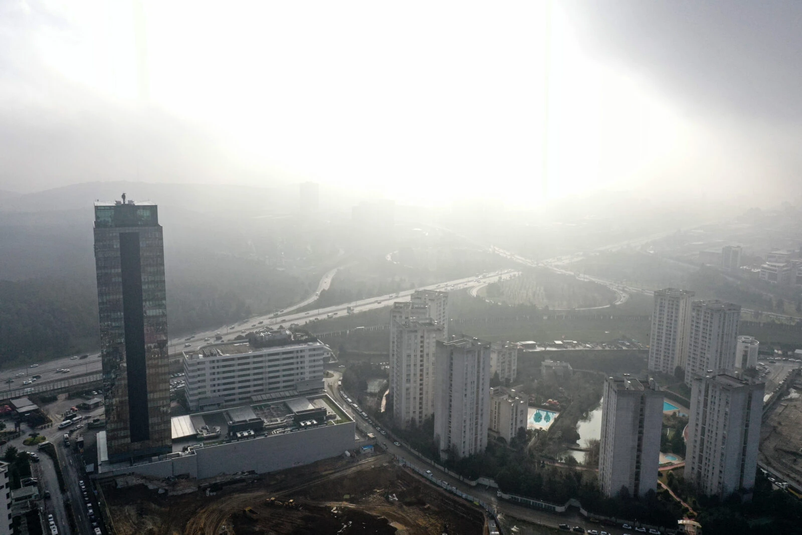 An aerial view of a foggy day in Istanbul, showing high-rise buildings, a highway with moving traffic, and residential complexes