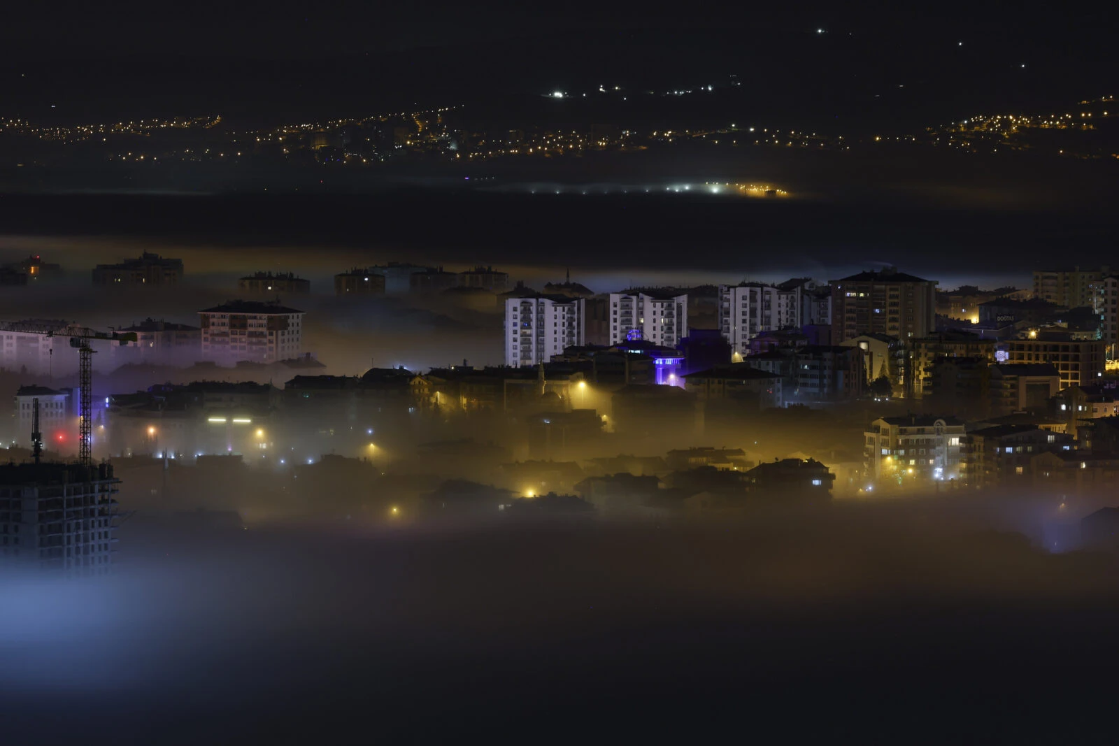 A thick layer of fog blankets the Turkish capital at night, partially obscuring buildings and streets while city lights glow through the mist