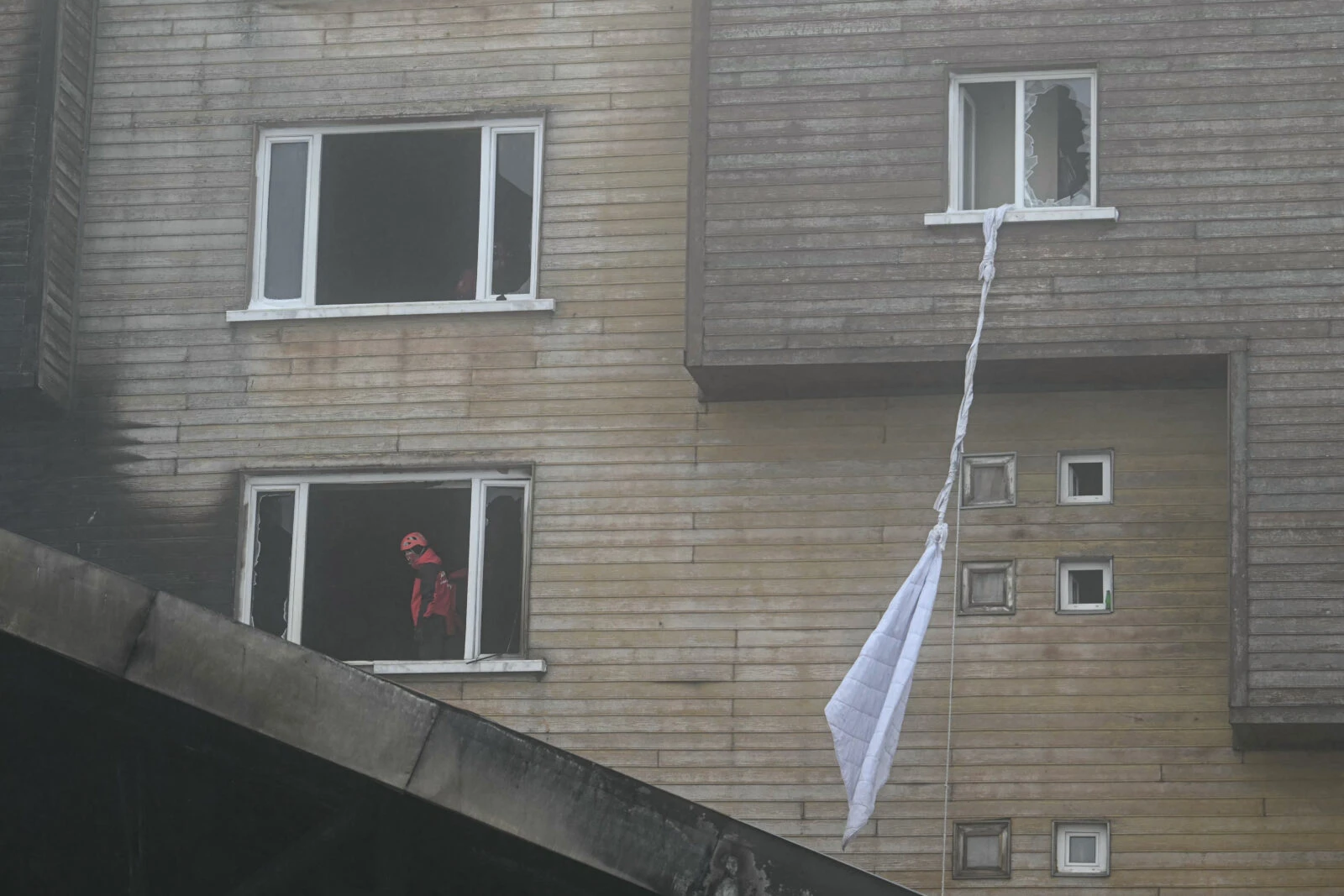 A Turkish rescue worker looks on from a room window next to a window with an attached bed sheet