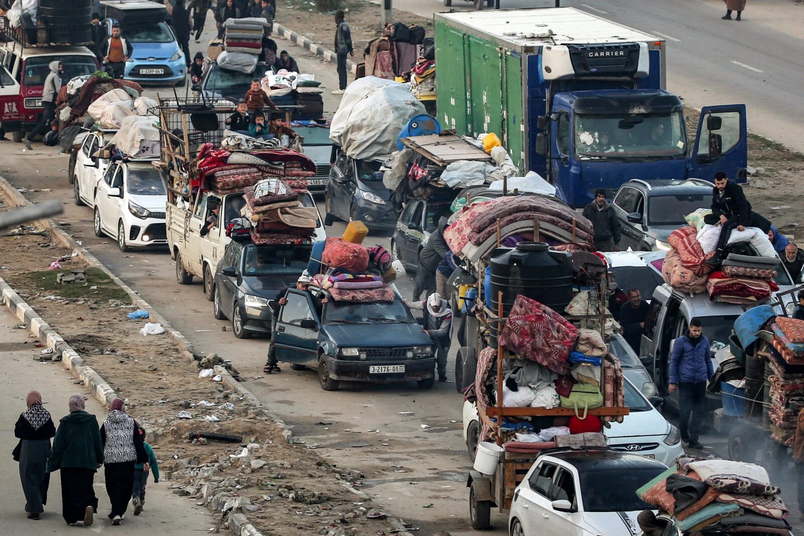 Three women walk past a queue of vehicles waiting 