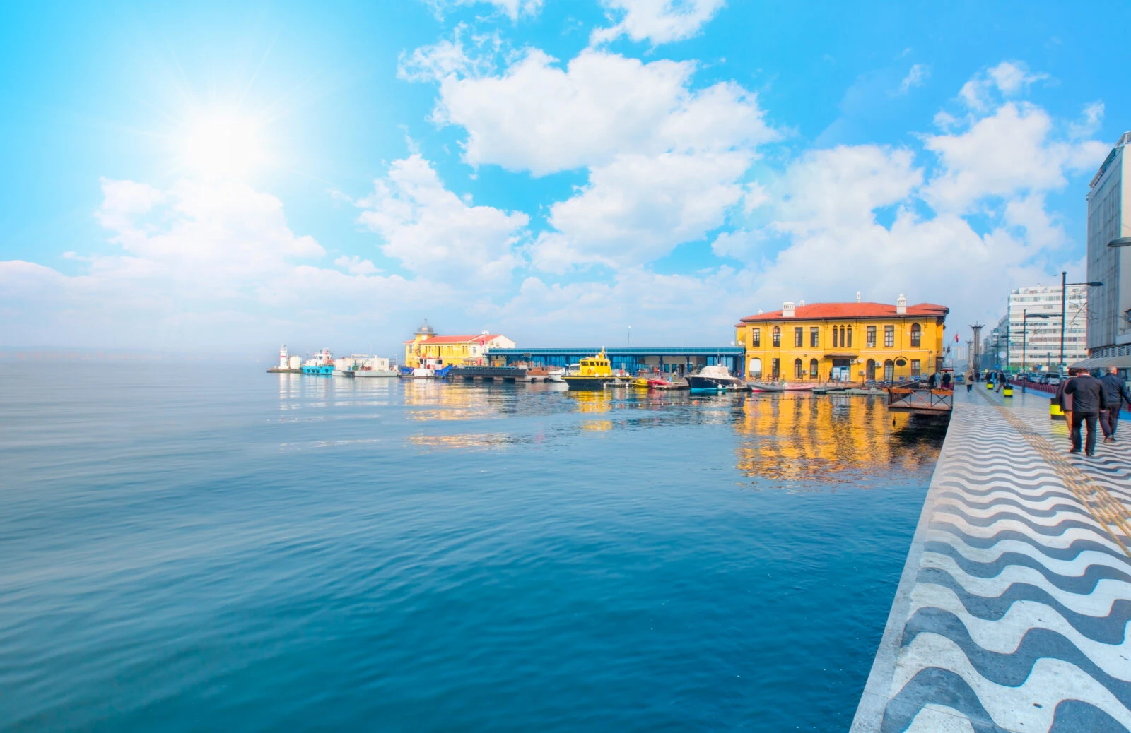 A sunny view of Izmir’s Kordon promenade, with blue waters, a clear sky, and historic architecture reflecting on the sea