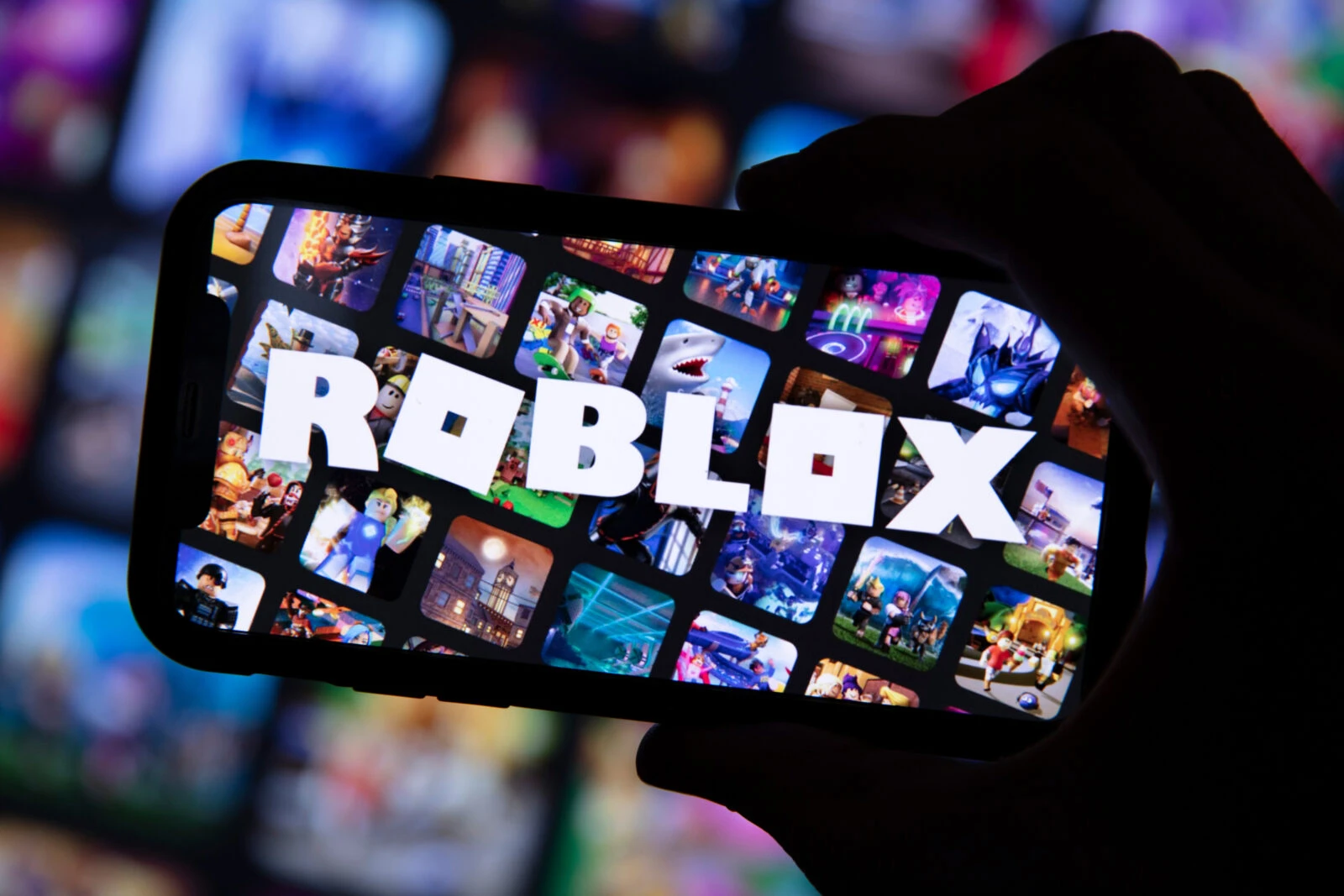 Photo shows a person holding a smartphone with Roblox game logo.