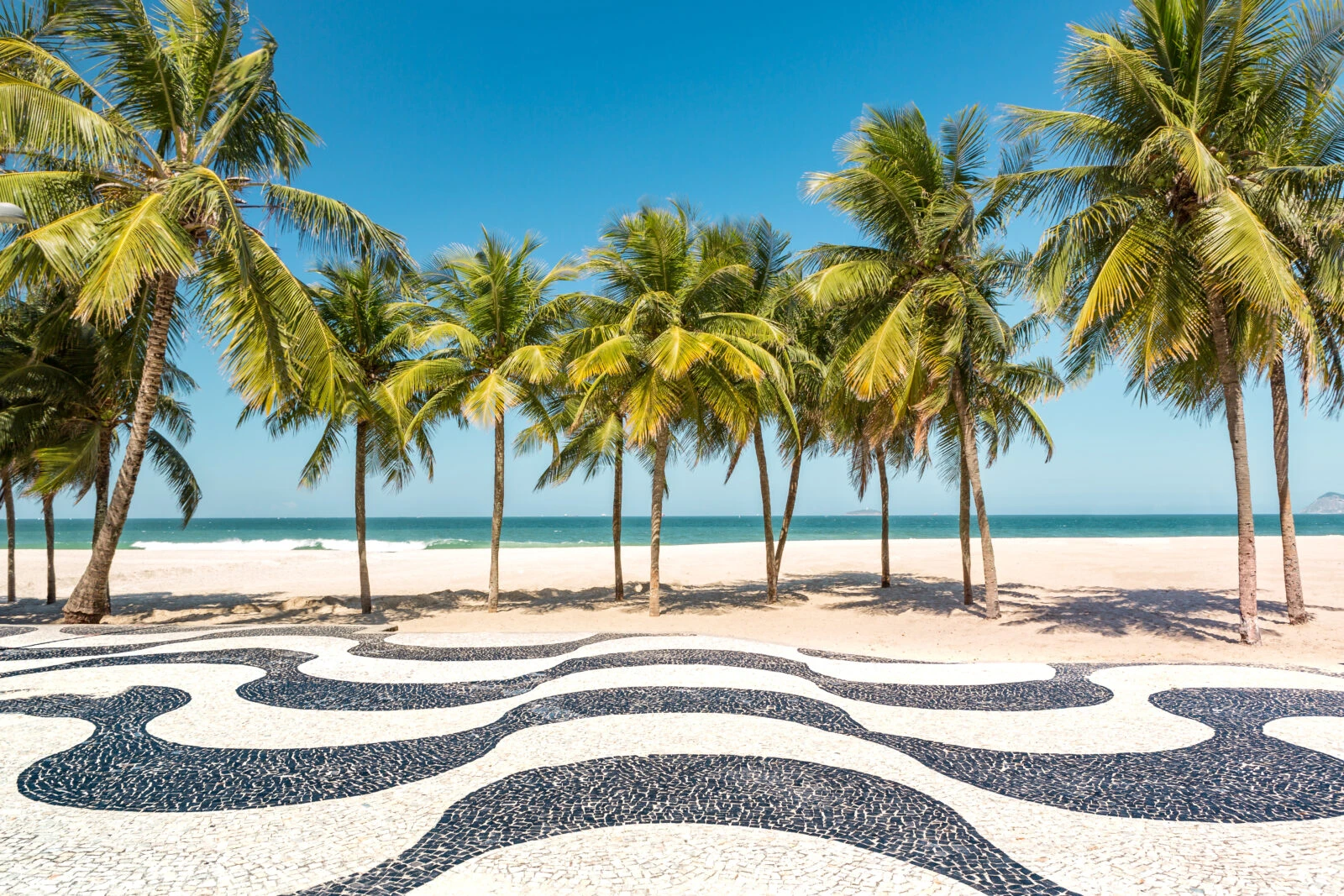 A scenic view of Copacabana Beach in Rio de Janeiro, Brazil, featuring black-and-white wave-patterned mosaics in the foreground, palm trees, and a bright blue sky