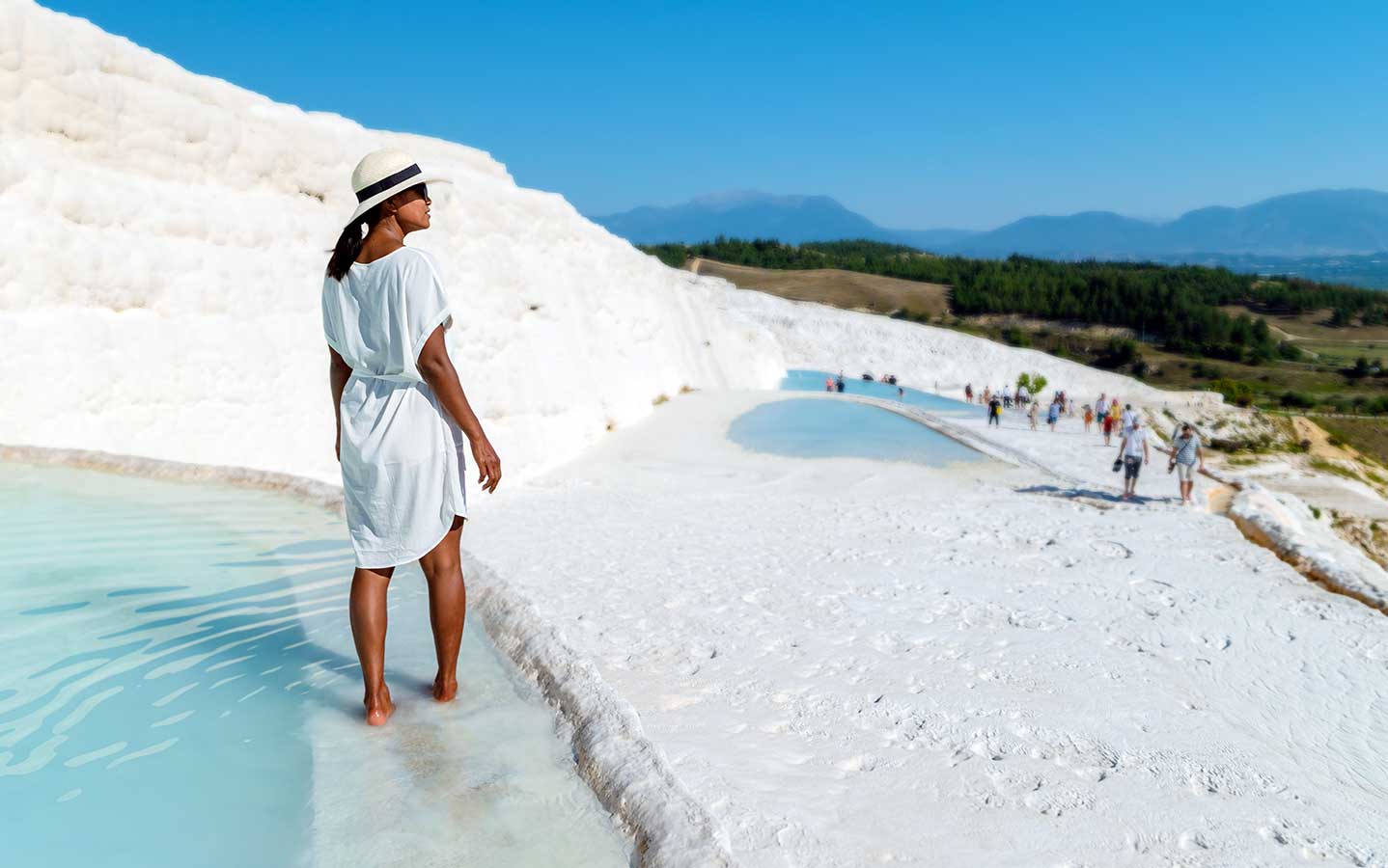  A woman stands in the crystal-clear travertine pools of Pamukkale, Türkiye, surrounded by white calcium-rich terraces.