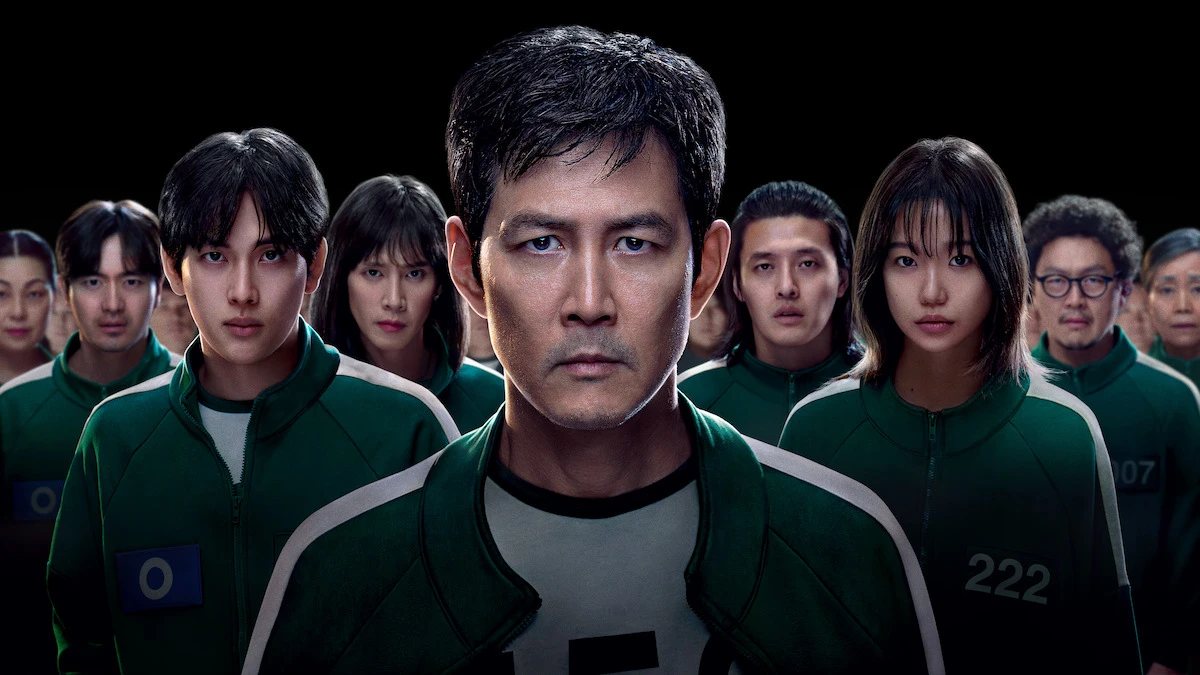 A promotional image of Netflix's Squid Game Season 2 shows a group of contestants dressed in green tracksuits, with a serious expression on their faces