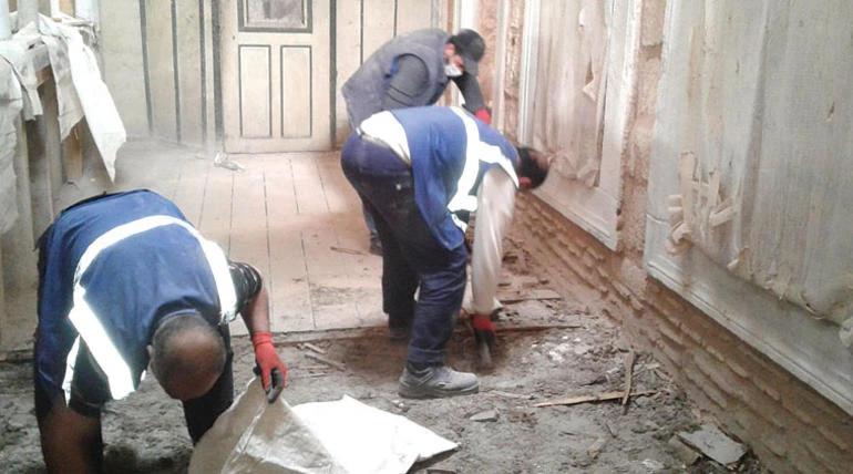 Three workers standing near removed floor tiles during restoration at Topkapı Palace.