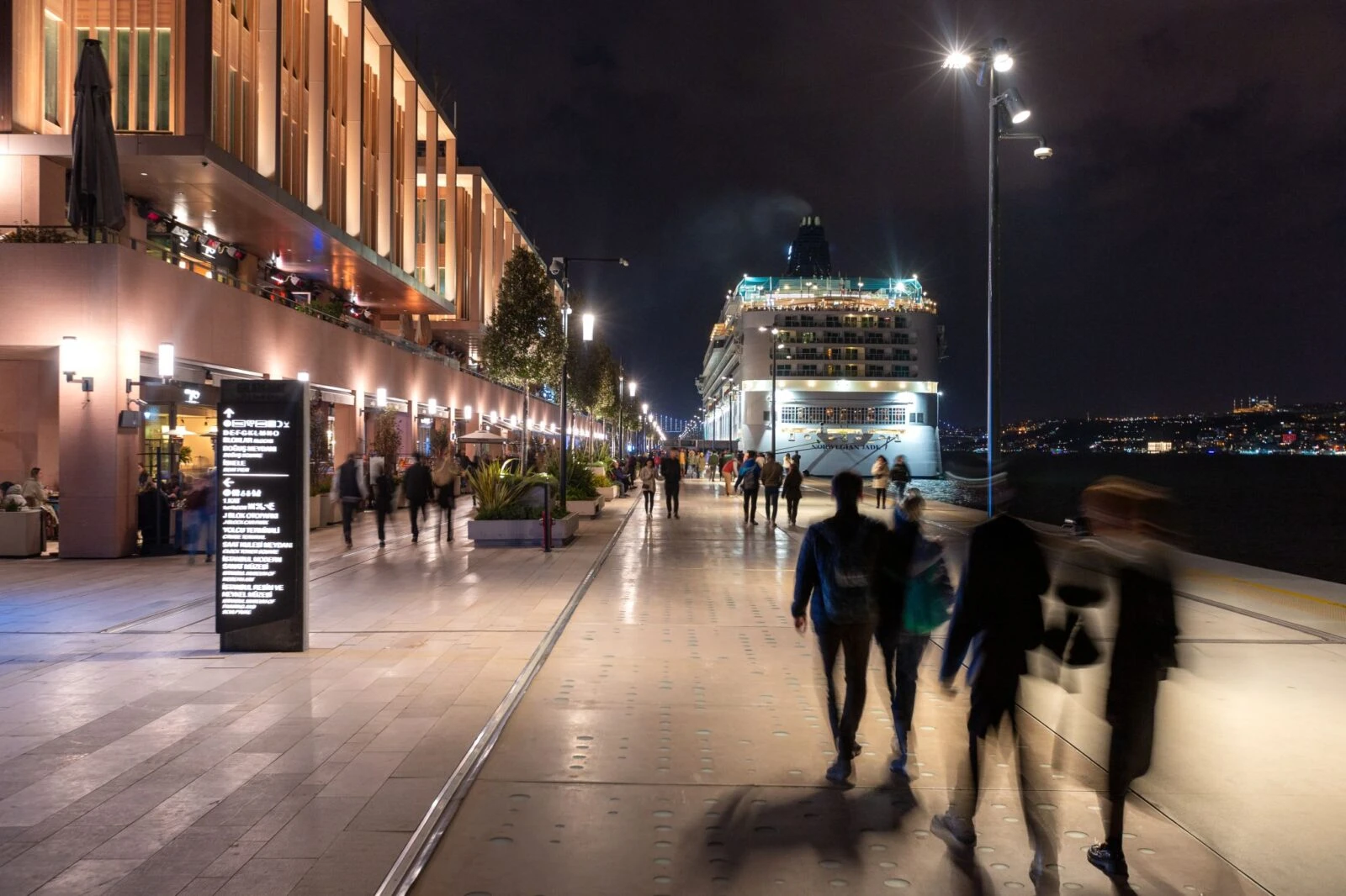 Passengers and visitors stroll along the illuminated promenade 