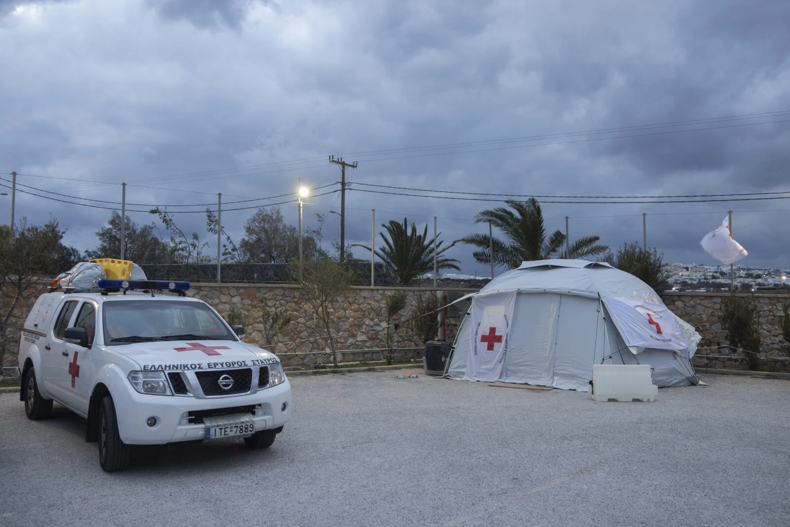 A Red Cross vehicle parked near a tent with a rescue dog standing nearby, part of an emergency response in Santorini, Greece.