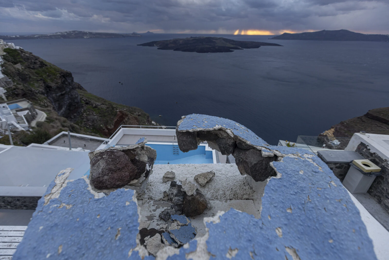 A damaged construction site with an empty pool and Nea Kammeni islet in the background on Santorini Island.