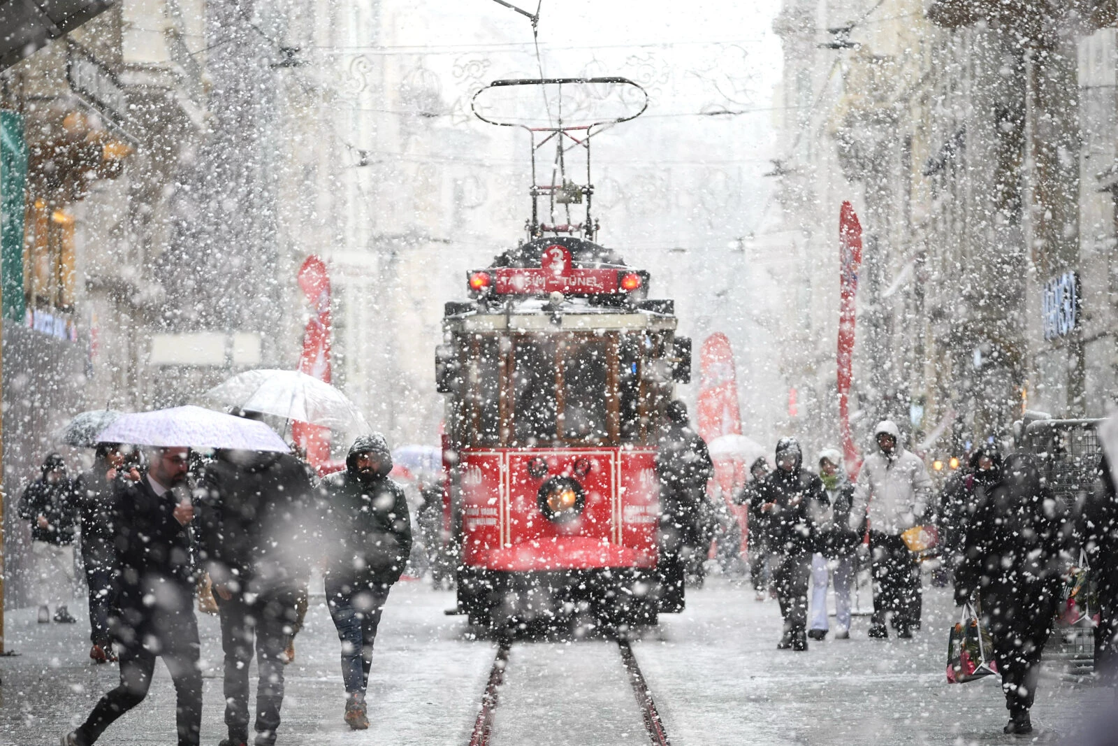 People walking with umbrellas on Istiklal Street while the nostalgic tram operates through the snow in Taksim, Istanbul.