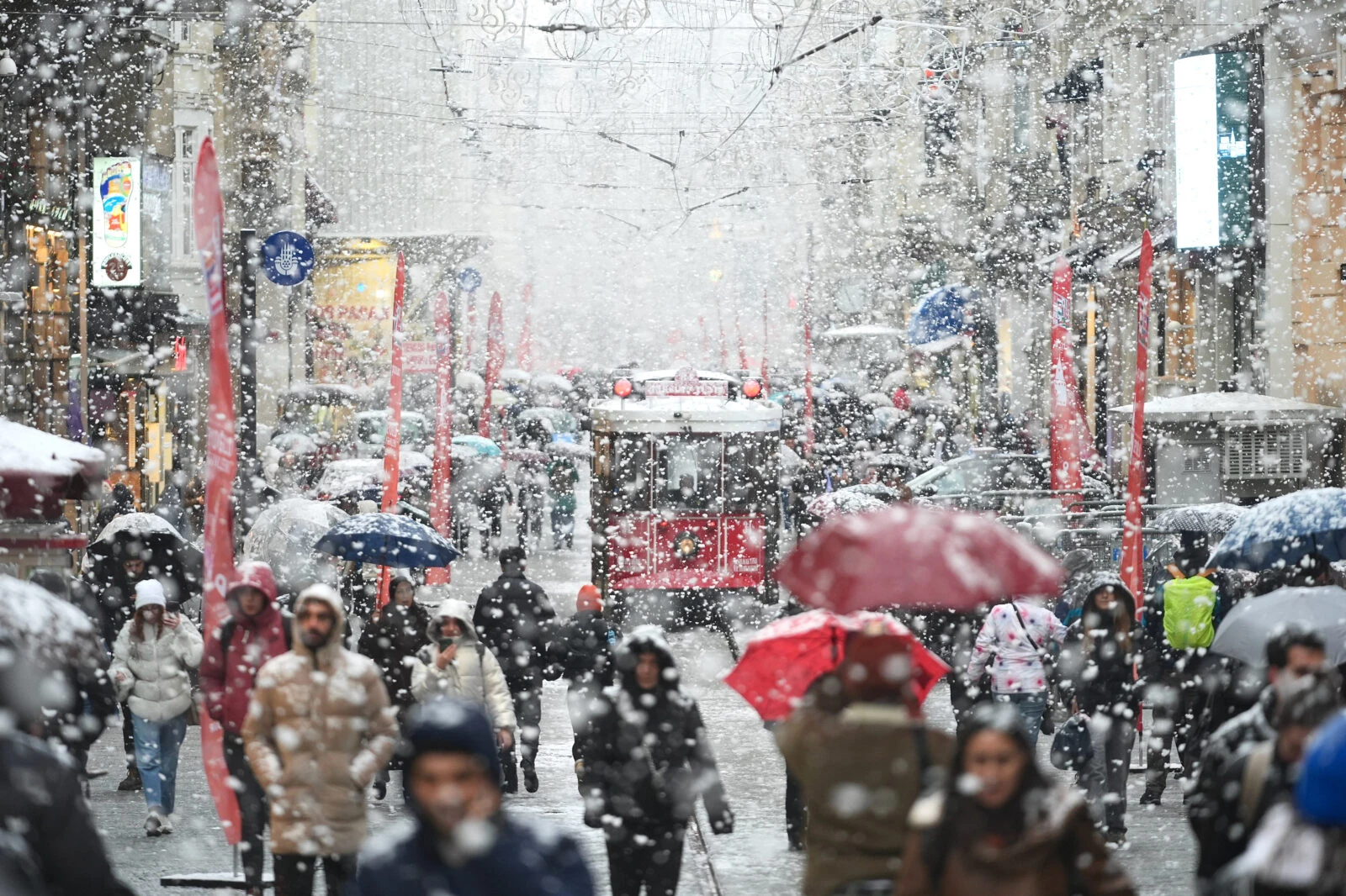 People with umbrellas walk along Istiklal Street while a nostalgic tram moves through the snowy Taksim area in Istanbul, Türkiye, on February 19, 2025.